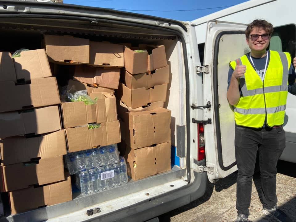 a support worker stands next to a trolly of supplies with his thumbs up